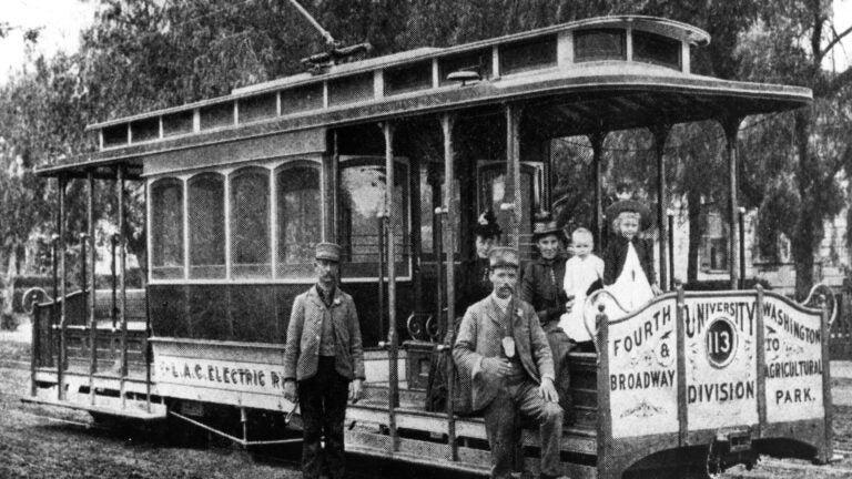 In black and white, men standing in front of a streetcar.